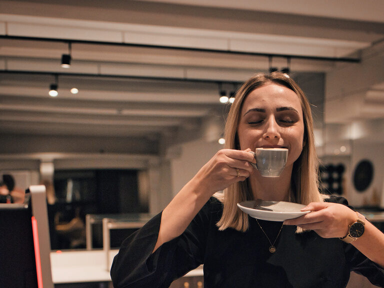 Eine Frau in einem modischen schwarzen Kleid genießt ihren Kaffee am Hotelbuffet im Hotel das Kronberg.