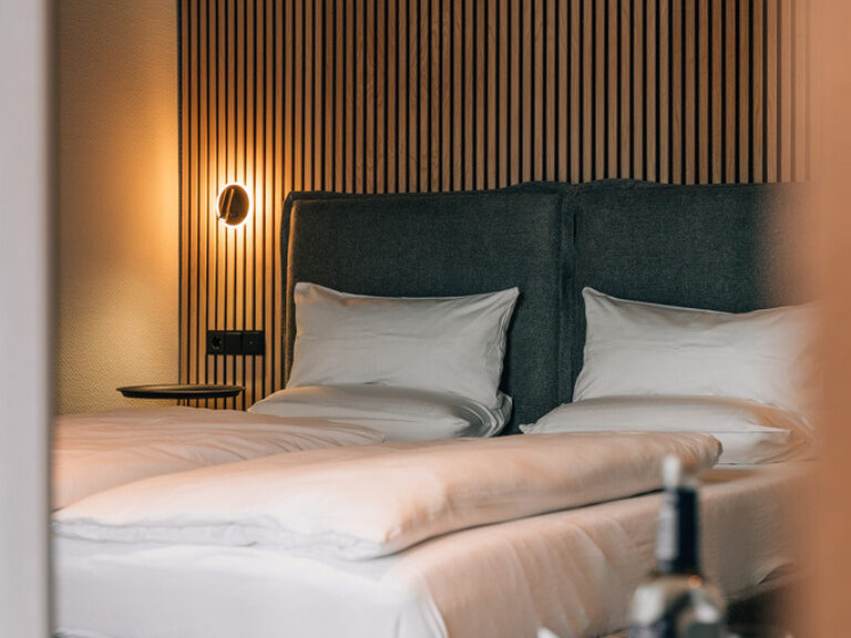 Ein gemütliches Zimmer mit Bett, Dekokissen und ambienter Beleuchtung.