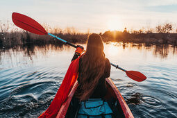 Eine Frau paddelt in der Abenddämmerung in einem roten Kajak auf den See hinaus.