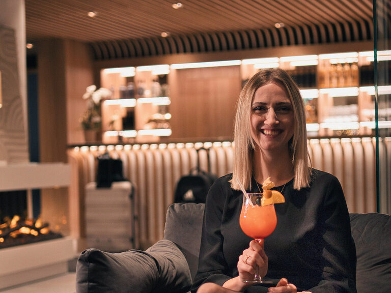 Auf einem stilvollen Sofa hält eine Frau ein Getränk in der Hand in der Lobby des Hotel Kronberg.