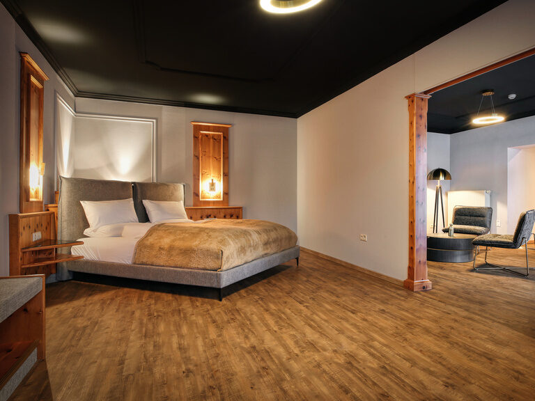 Ein elegantes Schlafzimmer mit Holzböden und großen Durchgang in den Wohnbereich im Hotel Kronberg.