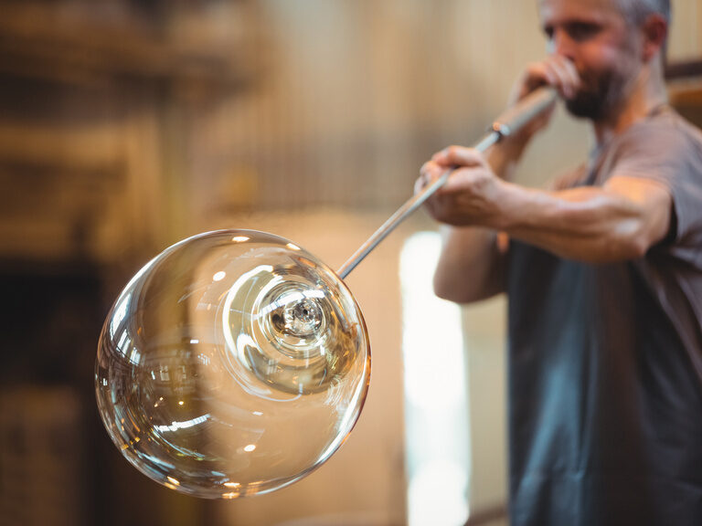 Ein Glasbläser formt eine Glaskugel.