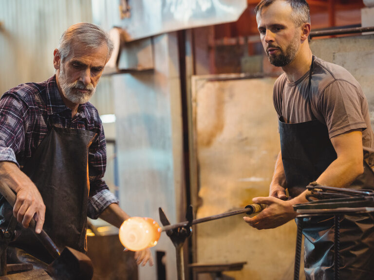 Zwei Männer bearbeiten gemeinsam das heiße Glas in der Werkstatt.
