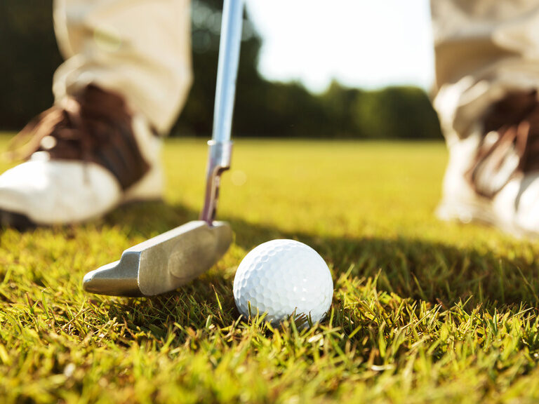 Ein Golfer mit Golfschläger und -ball steht auf einem gepflegten Golfplatz zum einputten bereit.