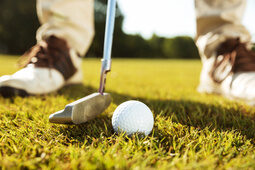 Ein Golfer mit Golfschläger und -ball steht auf einem gepflegten Golfplatz zum einputten bereit.