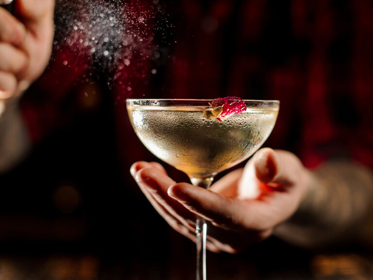 Hände halten ein Cocktail-Glas in der schicken Atmosphäre der Lifestyle-Bar im Hotel Kronberg in Bodenmais.