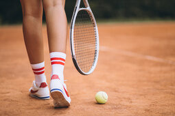 Die Füße eines Tennisspielers mit Schläger und Tennisball auf dem Sandplatz.