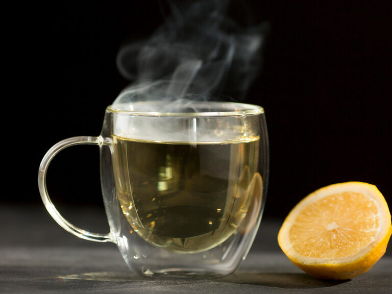 Eine Zitrone liegt neben einem dampfenden Glas mit heißem Tee.